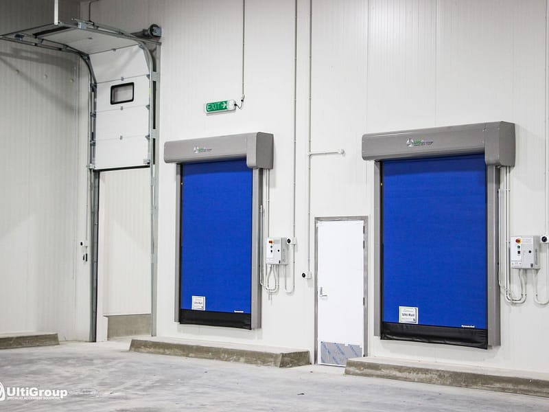 Two blue high-speed roll doors and a white sectional door in a warehouse.